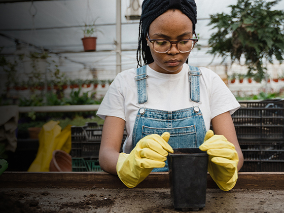 A woman wearing gloves while putting soil in a plant pot